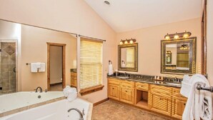 Un baño espacioso con una bañera grande, tocador de madera y varios espejos.