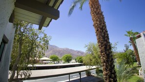 A view of a building with a palm tree in the foreground, a parking area, and mountains in the background.