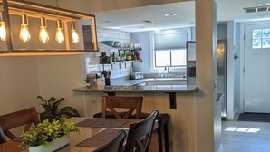 Een moderne keuken met een centraal eiland, een houten eettafel met stoelen en hangende lampen.