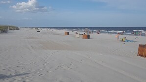Een breed zandstrand met enkele houten constructies en mensen in de verte.