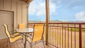 Een overdekt terras met een tafel en stoelen, een houten deur, en uitzicht op het landschap door een metalen hek.