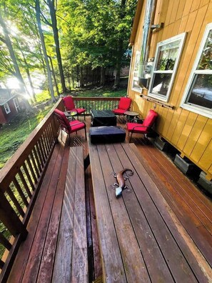 A wooden deck with red chairs and a table, surrounded by trees. - ***RUSTIC RETREAT***Peaceful, cozy cabin, with beautiful fall lake views (Carthage)
