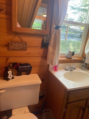A wooden cabin bathroom with a toilet, sink, and a welcome sign. - ***RUSTIC RETREAT***Peaceful, cozy cabin, with beautiful fall lake views (Carthage)