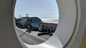 Blick durch ein Fenster auf eine Küstenstraße mit Häusern und einem Strand im Hintergrund.