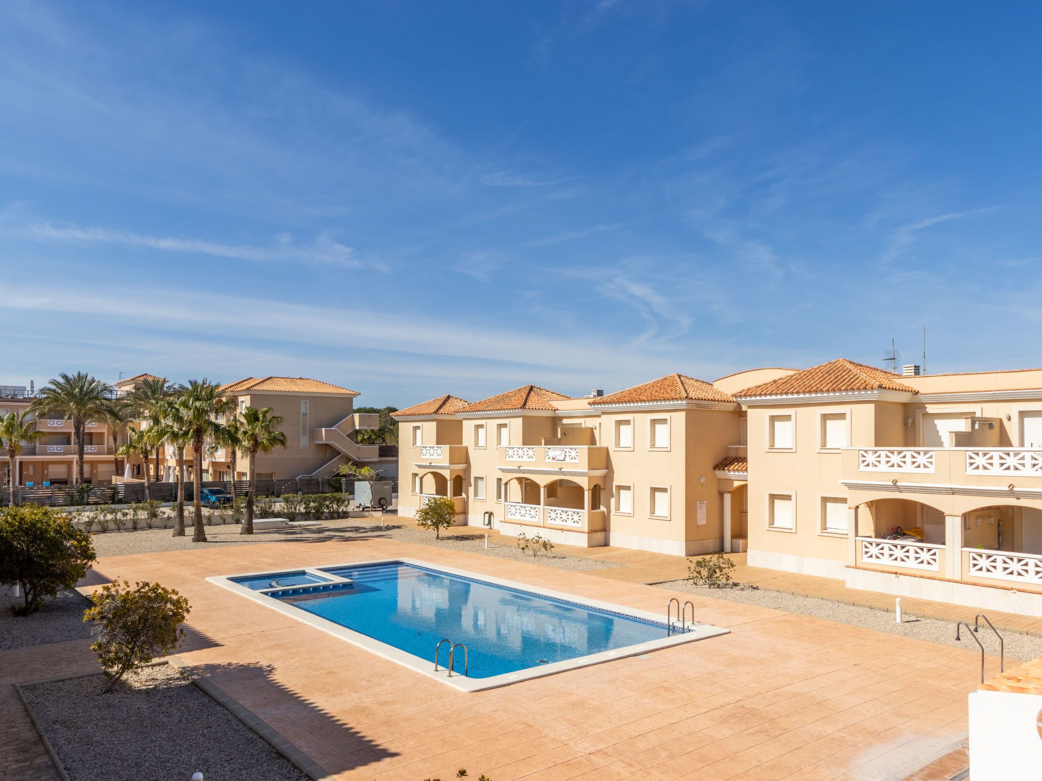 A hotel with a swimming pool, palm trees, and a clear blue sky.