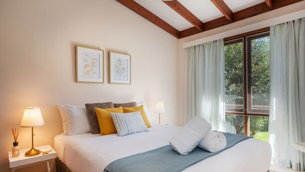 A bedroom with a large bed, two bedside tables, a window with curtains, and two framed botanical prints on the wall. - 8th Tee by Your Innkeeper Mudgee (Mudgee)