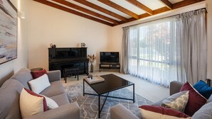 A living room with a sofa, a coffee table, a TV, and a piano. - 8th Tee by Your Innkeeper Mudgee (Mudgee)