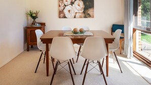 A dining area with a wooden table, four chairs, a painting of flowers, and a window with curtains. - 8th Tee by Your Innkeeper Mudgee (Mudgee)