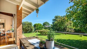 A balcony with a wooden table, two potted plants, and a view of a green lawn and trees. - 8th Tee by Your Innkeeper Mudgee (Mudgee)