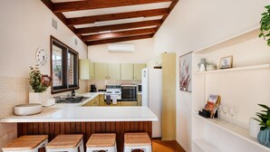 A kitchen with a central island, wooden stools, a clock, and a shelf with decorative items. - 8th Tee by Your Innkeeper Mudgee (Mudgee)