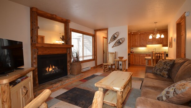 A cozy living room with a fireplace, wooden furniture, and a sofa. - Moose Ski Condo in Canyons Village of Park City 3-minutes from Slopes & Trails! (Park City)