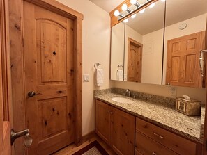 Un baño con armarios de madera, encimera de granito, lavabo y espejo con luces.