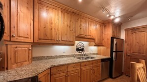 A kitchen with wooden cabinets, granite countertops, a stainless steel sink, and a black refrigerator. - Moose Ski Condo in Canyons Village of Park City 3-minutes from Slopes & Trails! (Park City)