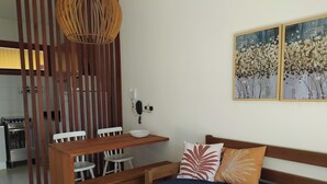 A modern living room with a wooden dining table, white chairs, a blue sofa with patterned cushions, and a decorative wall hanging. - Itacimirim Villages (Itacimirim)