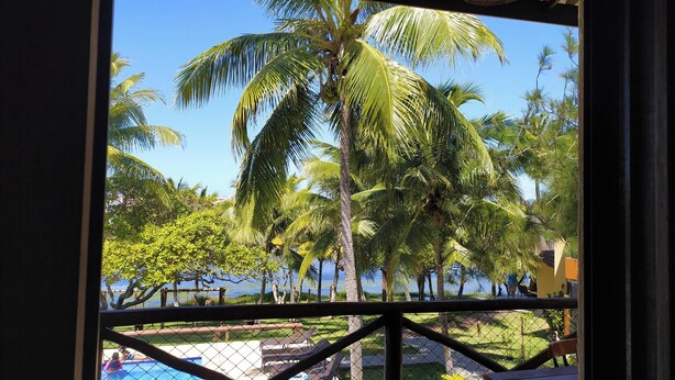 A pool area with palm trees and a view of the sea. - Itacimirim Villages (Itacimirim)