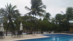 A swimming pool with lounge chairs and umbrellas, surrounded by palm trees. - Itacimirim Villages (Itacimirim)