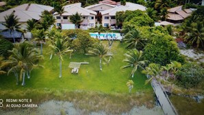 A large, multi-story building with a swimming pool surrounded by lush greenery and palm trees. - Itacimirim Villages (Itacimirim)