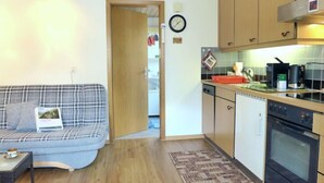 A compact living space with a sofa, a small table, a kitchen area with a stove, and a clock on the wall.