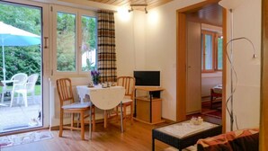 A cozy room with a wooden ceiling, a dining table with chairs, a TV, and a window with curtains.