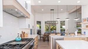 Une cuisine moderne dotée d’un îlot central, d’une cuisinière à gaz et de luminaires suspendus.