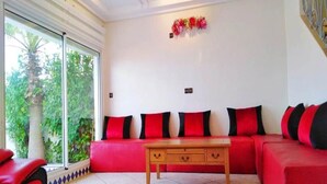 A living room with a red sofa, a wooden coffee table, and a large window with a view of greenery. - Summer Center Imi Ouaddar 5389 (Imi Ouaddar)