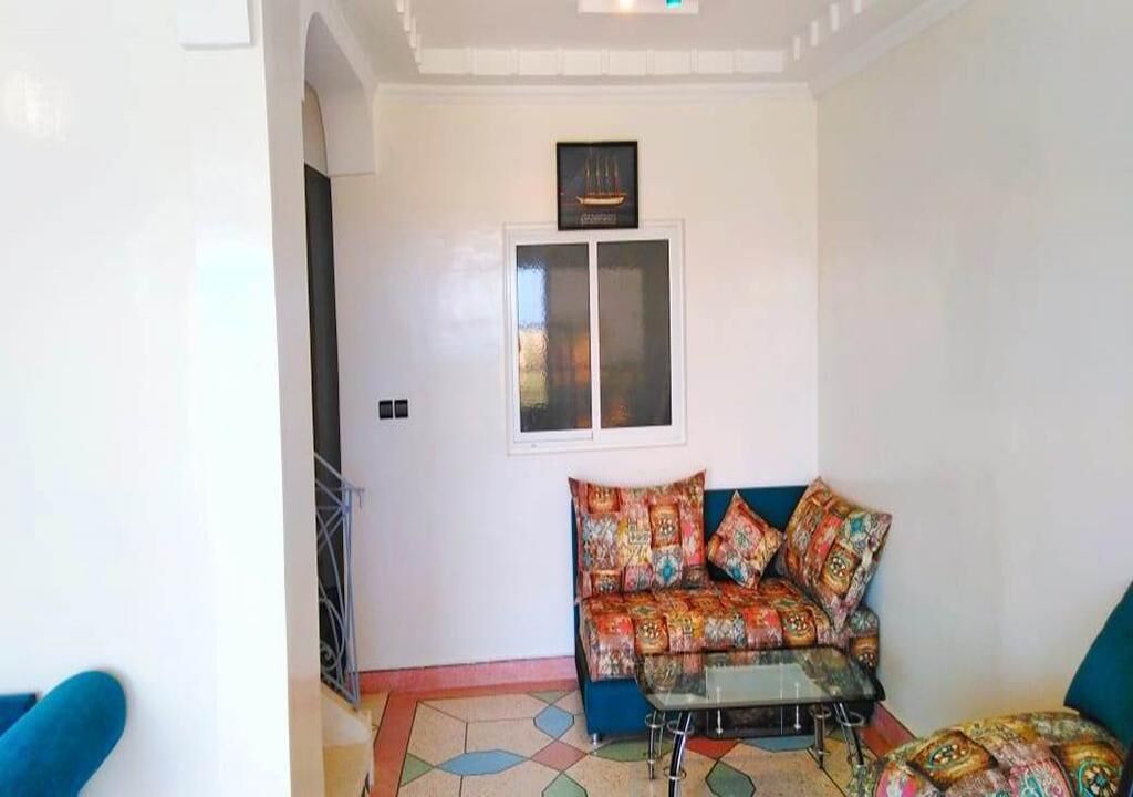 A living room with a sofa and a glass coffee table, a window with a picture frame, and a door.