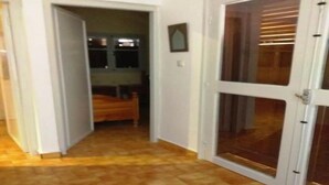 Un pasillo con piso de madera, una puerta blanca con paneles de vidrio y un pequeño cuadro en la pared.