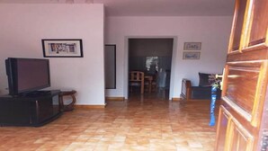 Una sala de estar con suelo de baldosas, un televisor sobre un mueble bajo y cuadros en la pared.