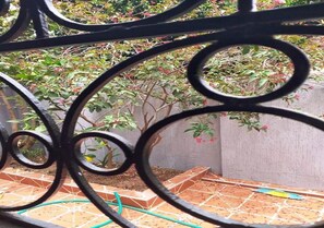 A courtyard with a tiled floor, a metal railing, and a plant with red flowers.