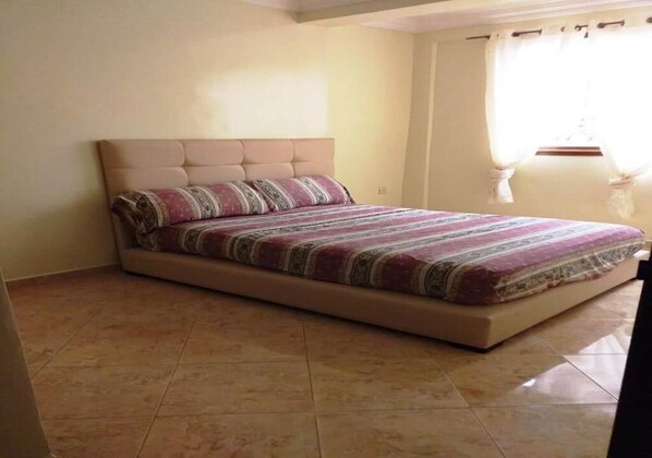 A bedroom with a bed, a headboard, and a window with curtains.