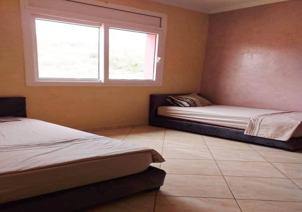 Ein Zimmer mit zwei Betten, einem Fenster und einer schlichten Wand.
