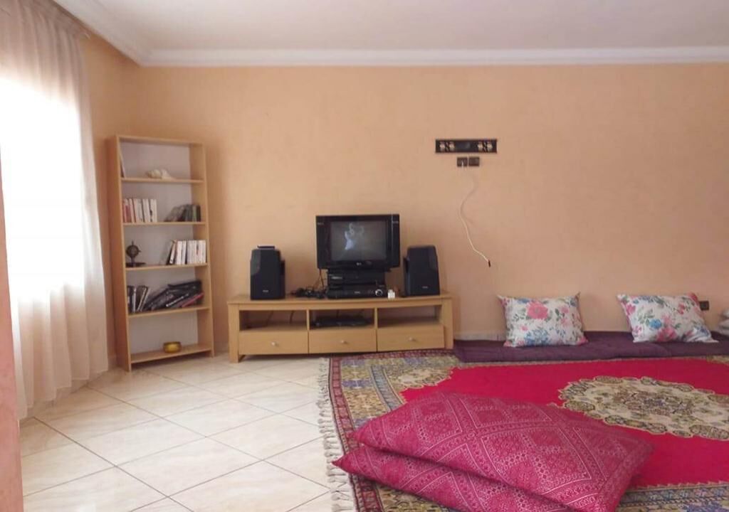 A living room with a television on a wooden stand, a bookshelf, and a patterned rug.