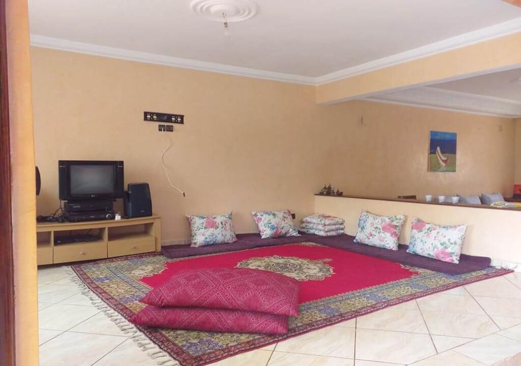 A living room with a television on a wooden stand, a patterned rug, and a sofa with floral cushions.