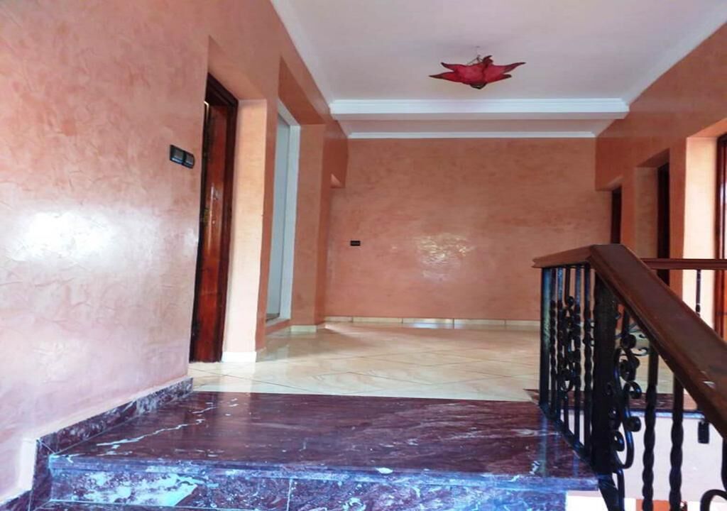 Un couloir avec un escalier en marbre, une rampe en bois et un luminaire au plafond.