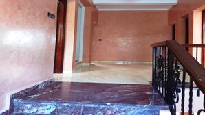Un couloir avec un escalier en marbre, une rampe en bois et un luminaire au plafond.
