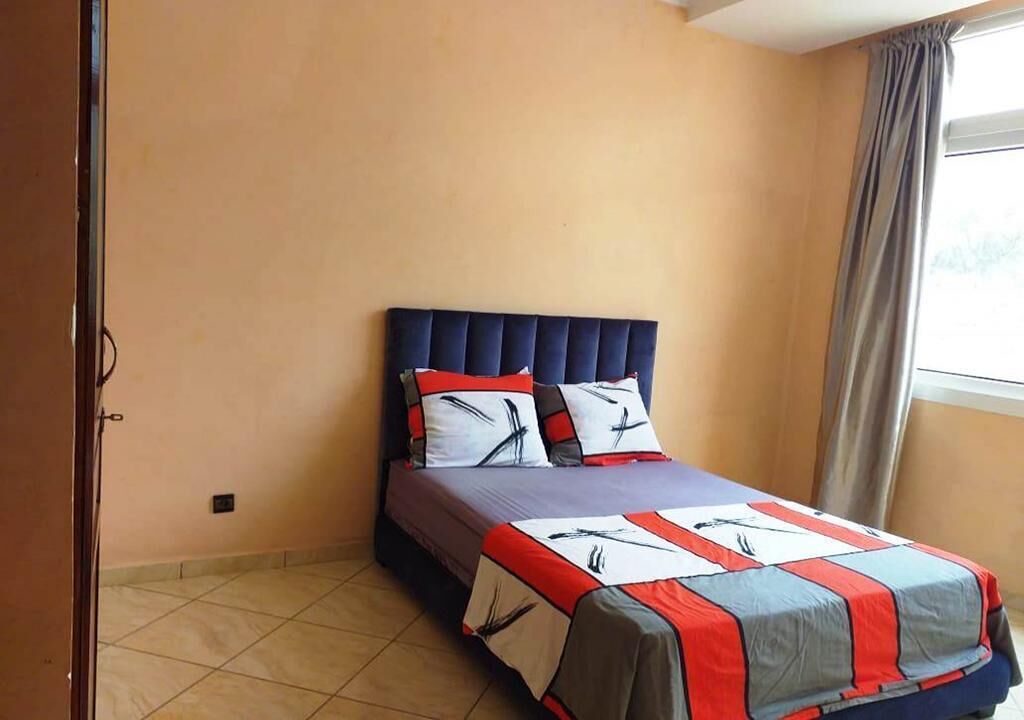 Un dormitorio con cama, cabecera y ventana con cortinas.