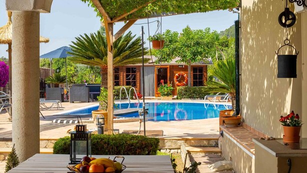 A pool area with a view of a house, outdoor seating, and a table with fruit. - Beautiful finca with pool in Selva, in the center of Mallorca. (Selva)