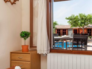 A room with a window overlooking a pool and a building with a red roof.