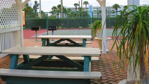 Un área de picnic cubierta con bancos y una cancha de tenis al fondo.