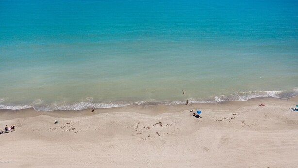 Una playa con agua turquesa cristalina, una orilla arenosa y algunas personas con sombrillas.