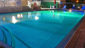 Una piscina interior con una terraza de madera, sillas de descanso y una valla blanca.