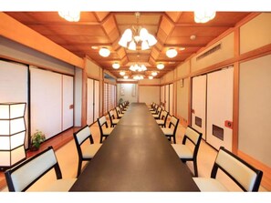 Conference room with a long table and rows of chairs, featuring traditional Japanese sliding doors and recessed lighting.