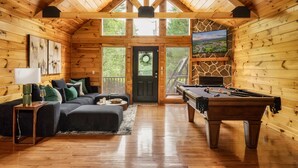 Ein gemütliches Blockhaus-Interieur mit Holzbalkendecke, Billardtisch, einer Couch und einem Fernseher.