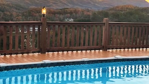 Una terraza de madera con piscina, con vista a un paisaje montañoso.