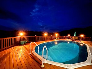 Piscina em deck de madeira com guarda-corpos e iluminação, cercada por uma paisagem montanhosa.