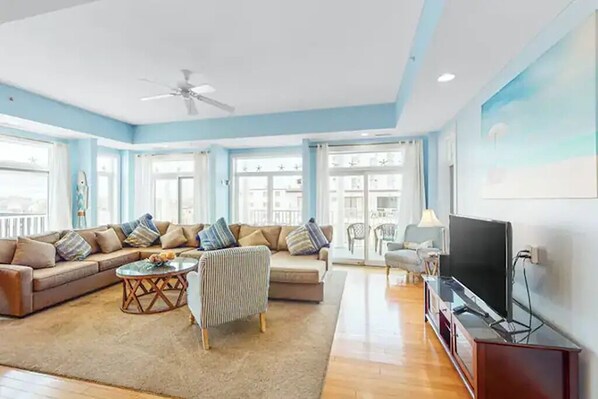 A spacious living room with a sofa set, a television, and a ceiling fan.