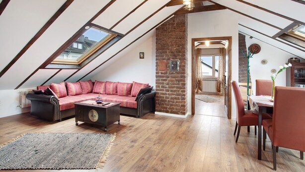 A loft-style room with a sloped ceiling, a red sofa, a dining table with chairs, and a brick accent wall. - Apartment "Haus Elena Wohnung 7A" with Mountain View, A/C, Wi-Fi, Garden & Terrace (Bestwig)
