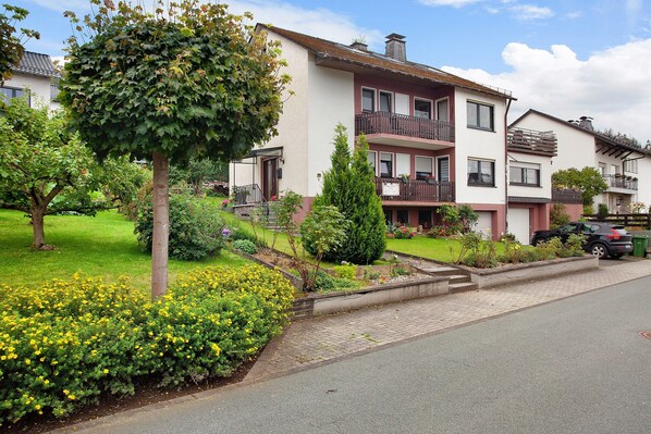 Un immeuble résidentiel doté d’un jardin, d’un arbre et d’une allée pavée.