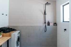 Un área de lavandería con lavadora, un tendedero y un cabezal de ducha montado en una pared de azulejos.