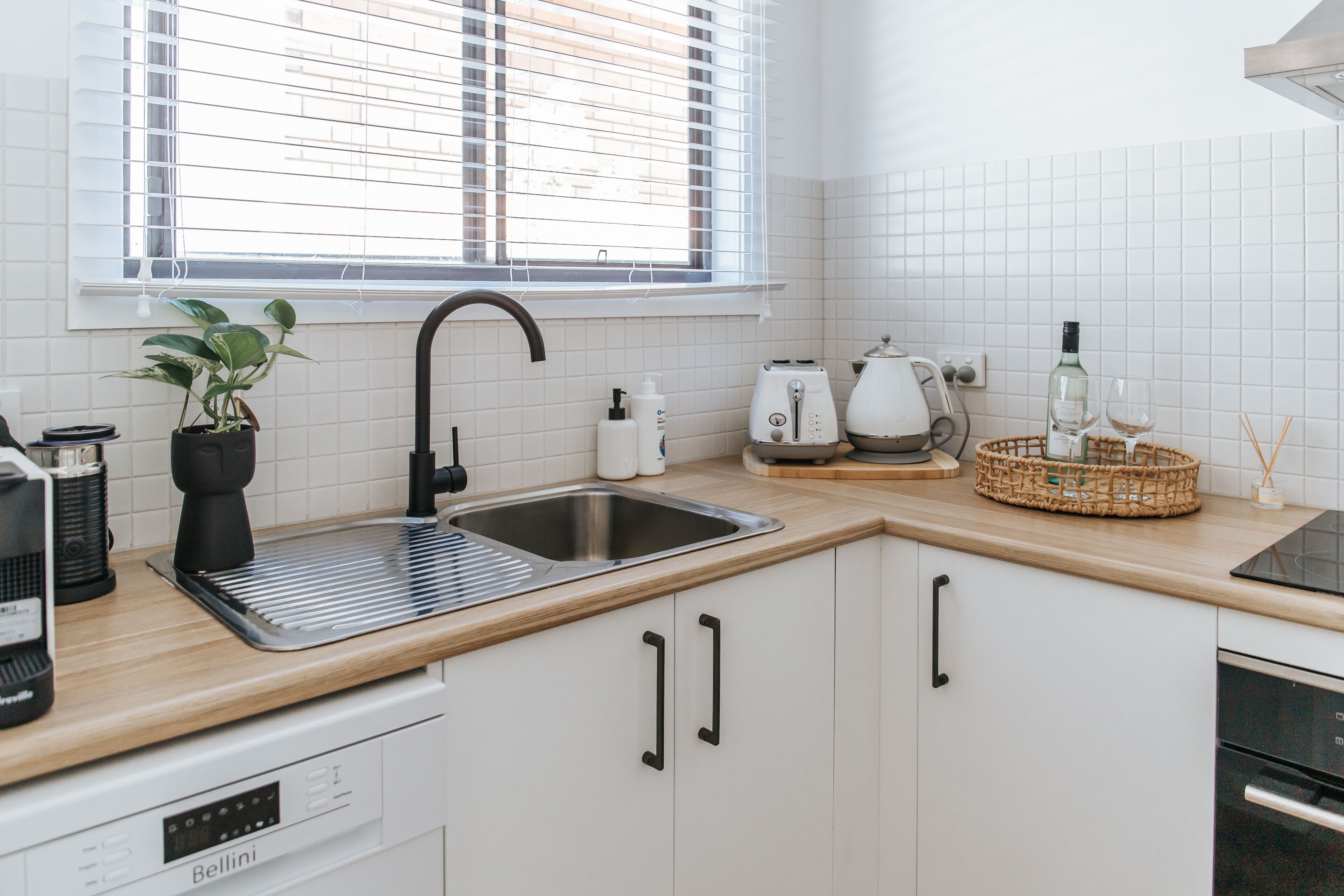 Een moderne keuken met witte kasten, een roestvrijstalen spoelbak, een broodrooster en een koffiezetapparaat.